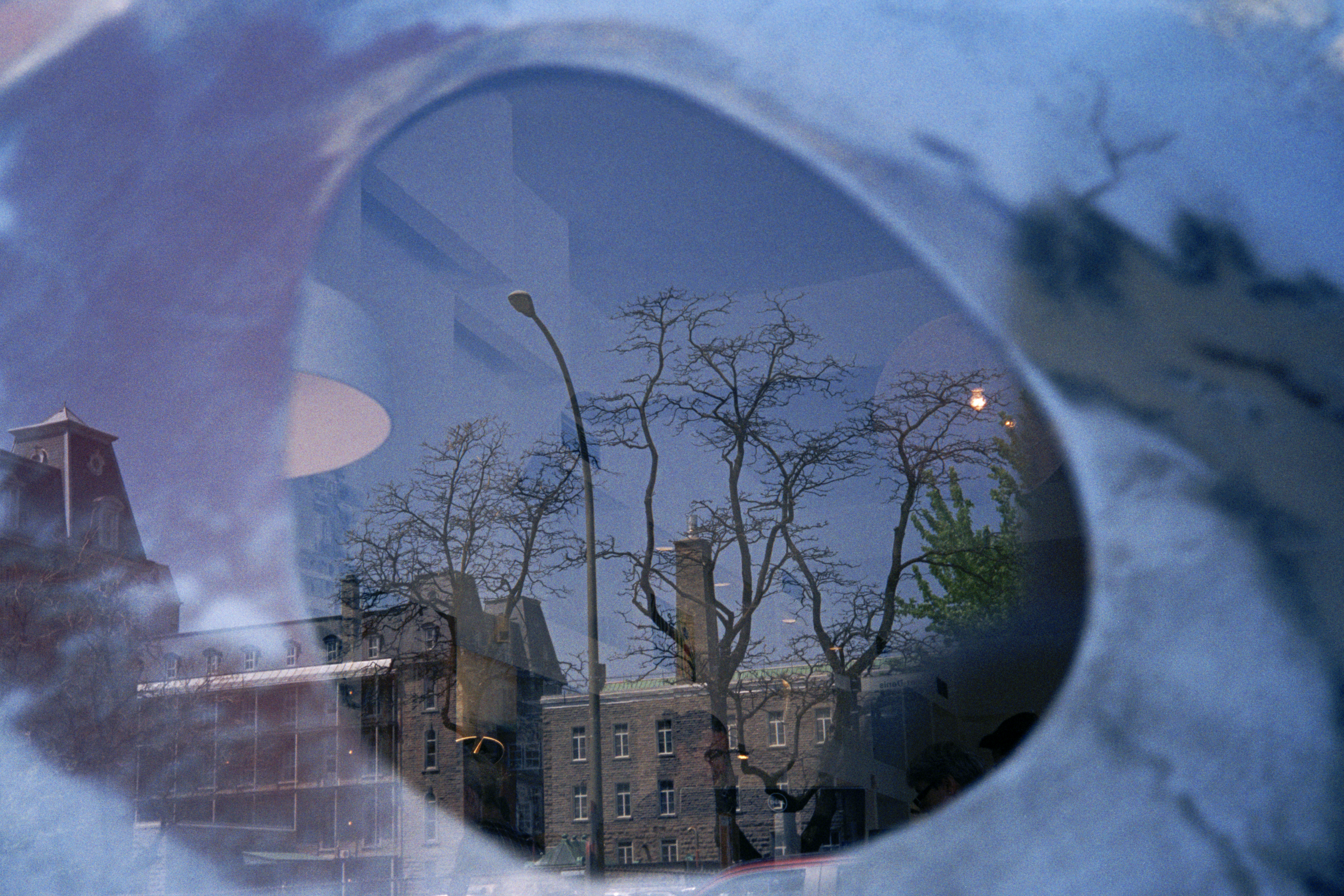 La photographie montre une fenêtre de bâtiment avec une vue sur des arbres et des bâtiments en arrière-plan. La fenêtre es...